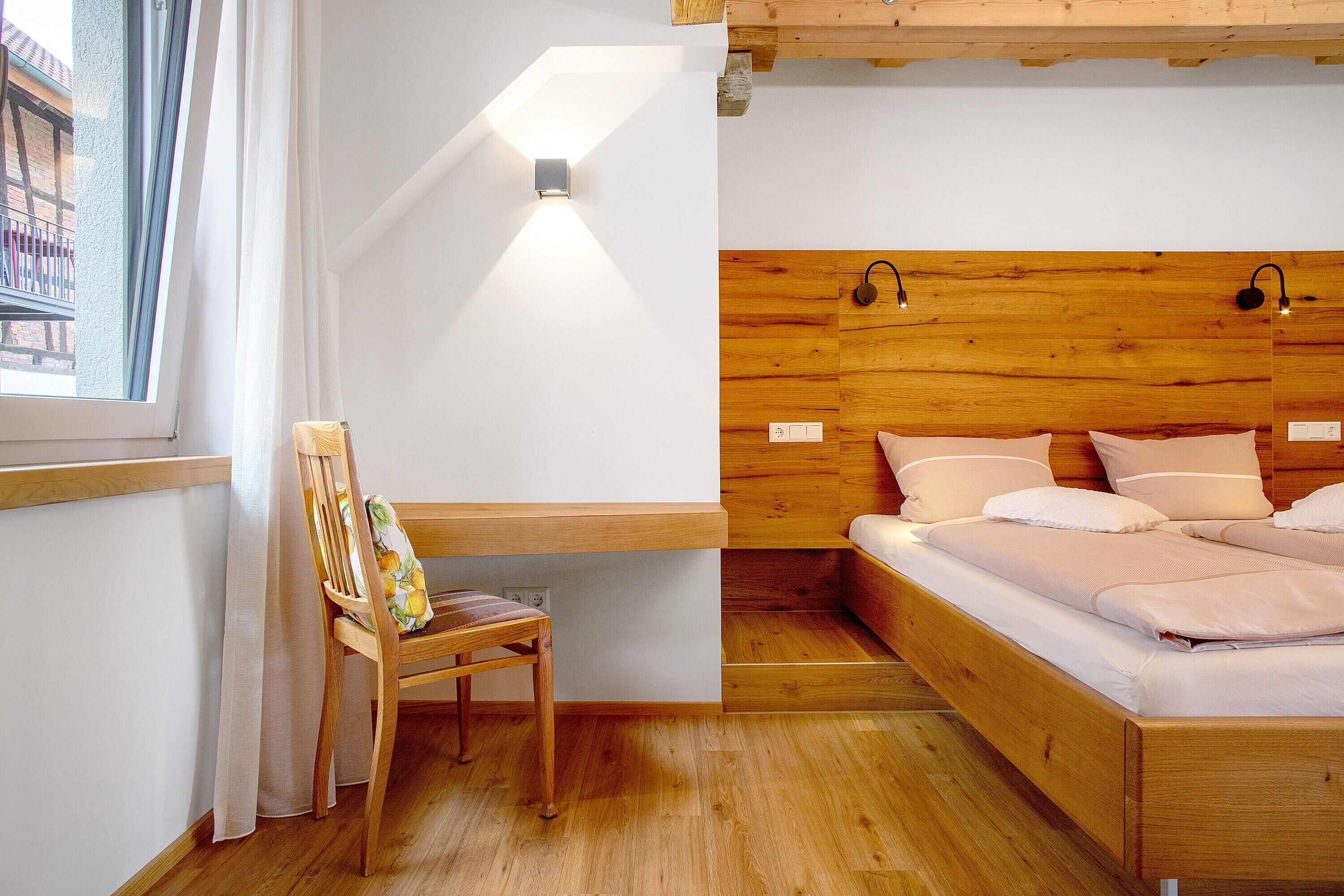 Une chambre à coucher avec une tête de lit en bois, une table de chevet, une chaise et une fenêtre avec des rideaux.