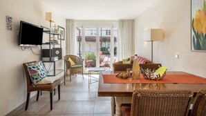 Une chambre meublée comprenant une table à manger, des chaises, un téléviseur et une vue sur l’extérieur, visible à travers une porte vitrée.