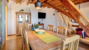 A dining area with a wooden table, chairs, a television, and a staircase. - Apartment "Kornboden" with Shared Garden, Balcony, and Wi-Fi (Immenstaad am Bodensee)