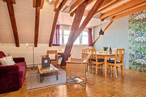 A cozy room with wooden beams, a dining table with chairs, a red sofa, and a laptop on a small table.
