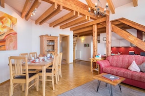 A dining area with wooden chairs and a table, a red sofa, and a staircase leading to an upper level.