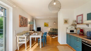 Een moderne keuken met houten vloeren, een eethoek met een witte tafel en blauwe stoelen, en een groot raam.