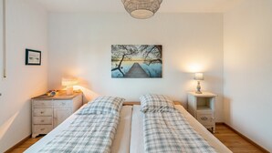 Een slaapkamer met twee bedden, een nachtkastje met een lamp, een schilderij aan de muur en een hanglamp.