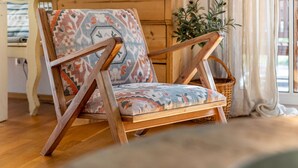 Een houten stoel met een gestreept kussen, een houten tafel, een rieten mand en een plant in een kamer met een houten vloer en een raam met gordijnen.
