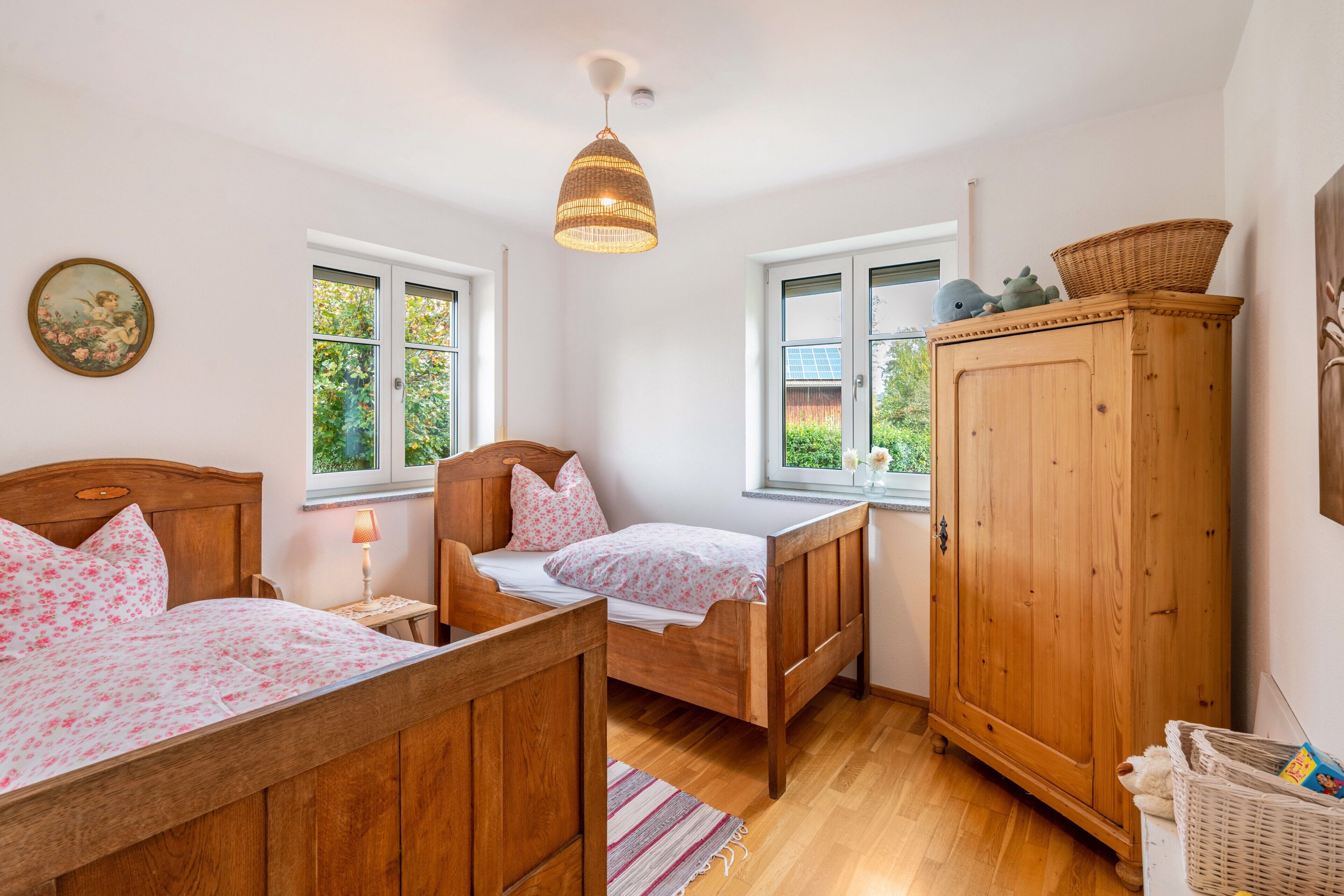 Une chambre à coucher avec deux lits en bois, une armoire en bois et une fenêtre donnant sur un paysage verdoyant.