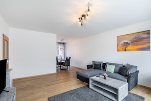 A modern living room with a grey sofa, a coffee table, and a dining area in the background.