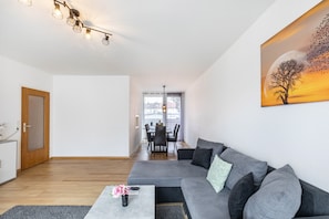 Ein modernes Wohnzimmer mit einem grauen Ecksofa, einem kleinen Couchtisch und einem Baumgemälde.