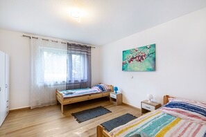 A bedroom with a bed, a nightstand, a window with curtains, a radiator, and a painting on the wall.