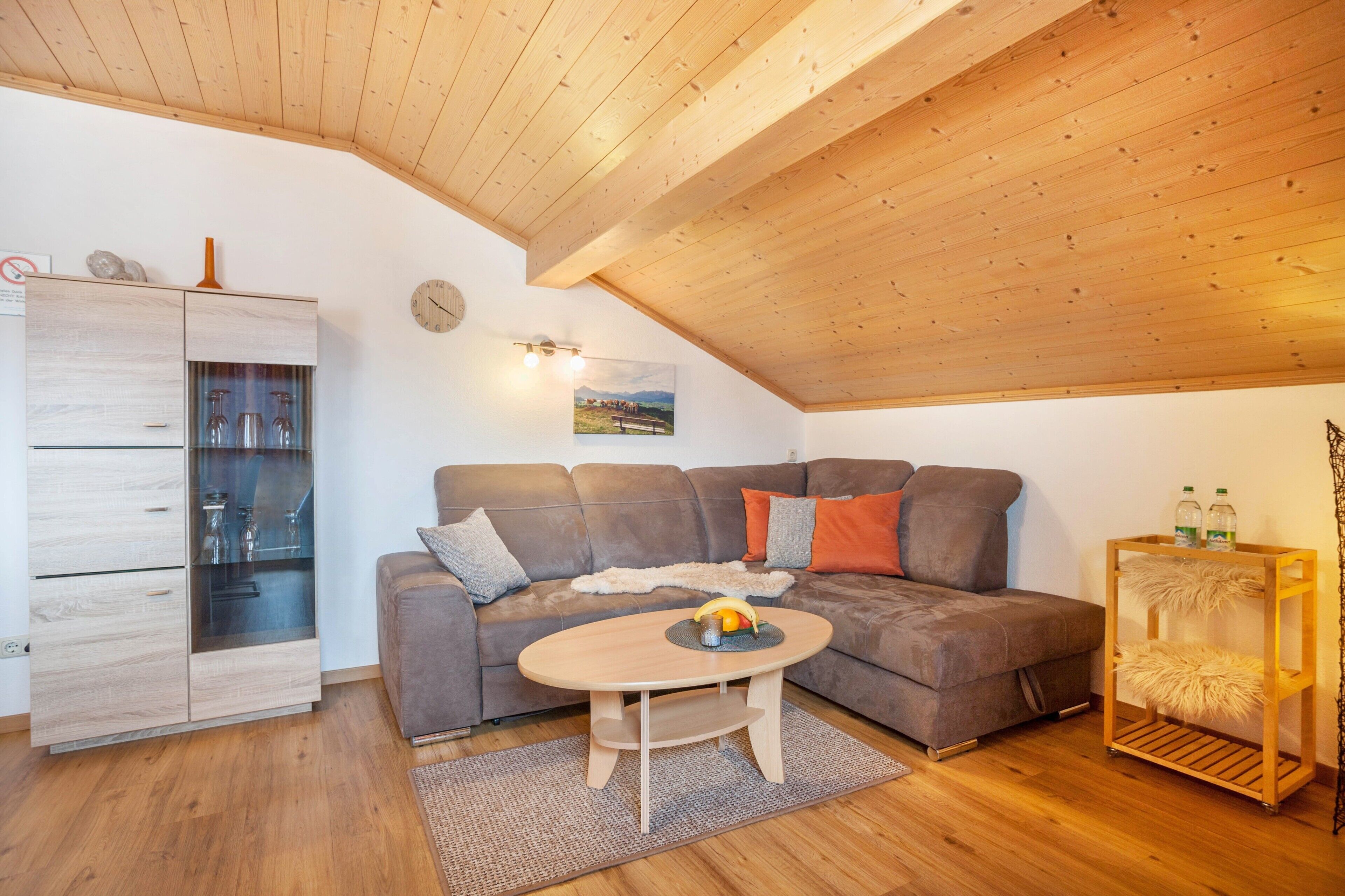 Um espaço de estar estilo loft acolhedor, com teto de madeira, um sofá de couro marrom, um armário de madeira e uma pequena mesa redonda com uma fruteira.