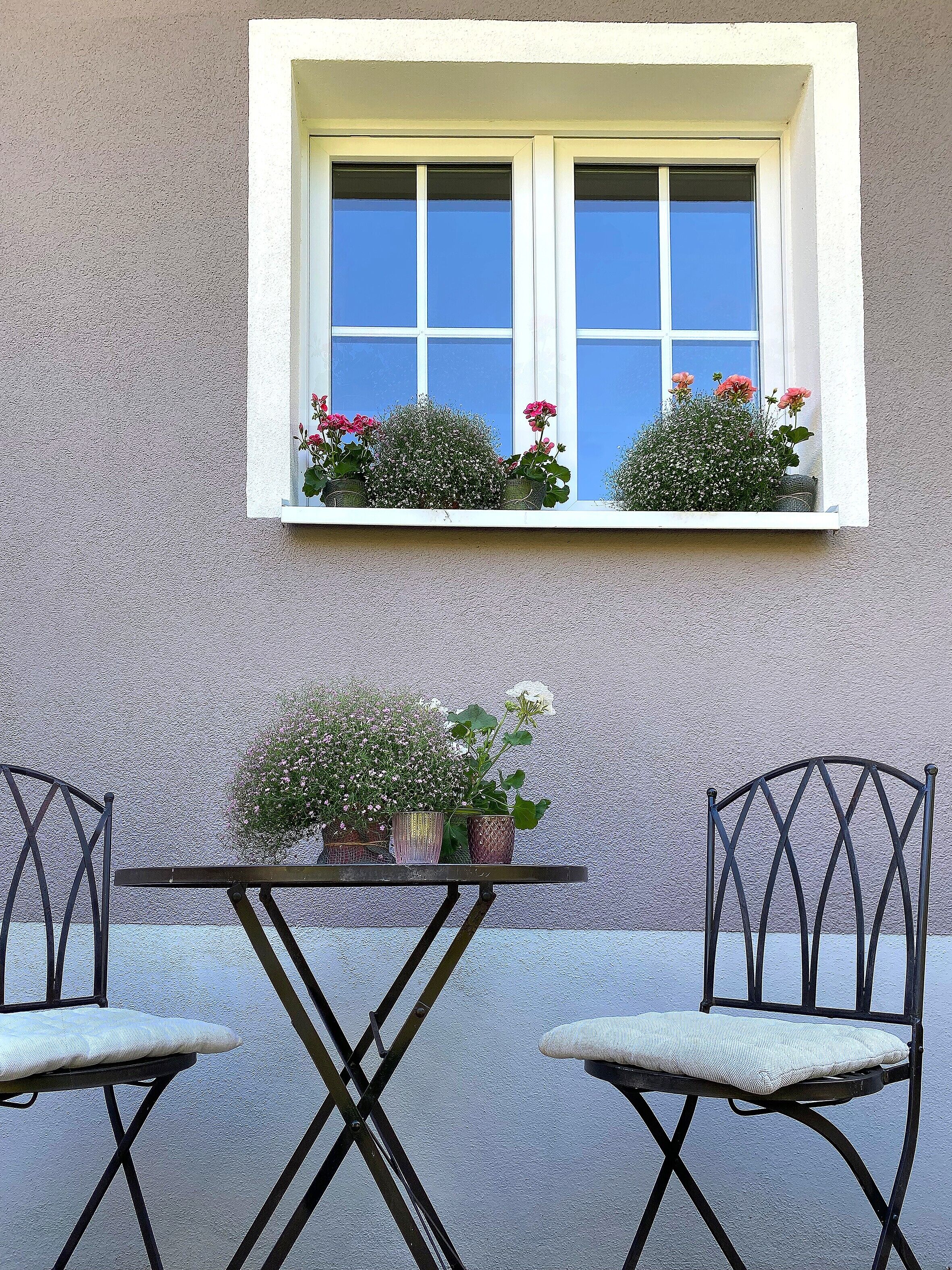 A window with white frames, two potted plants, and a table with two chairs.