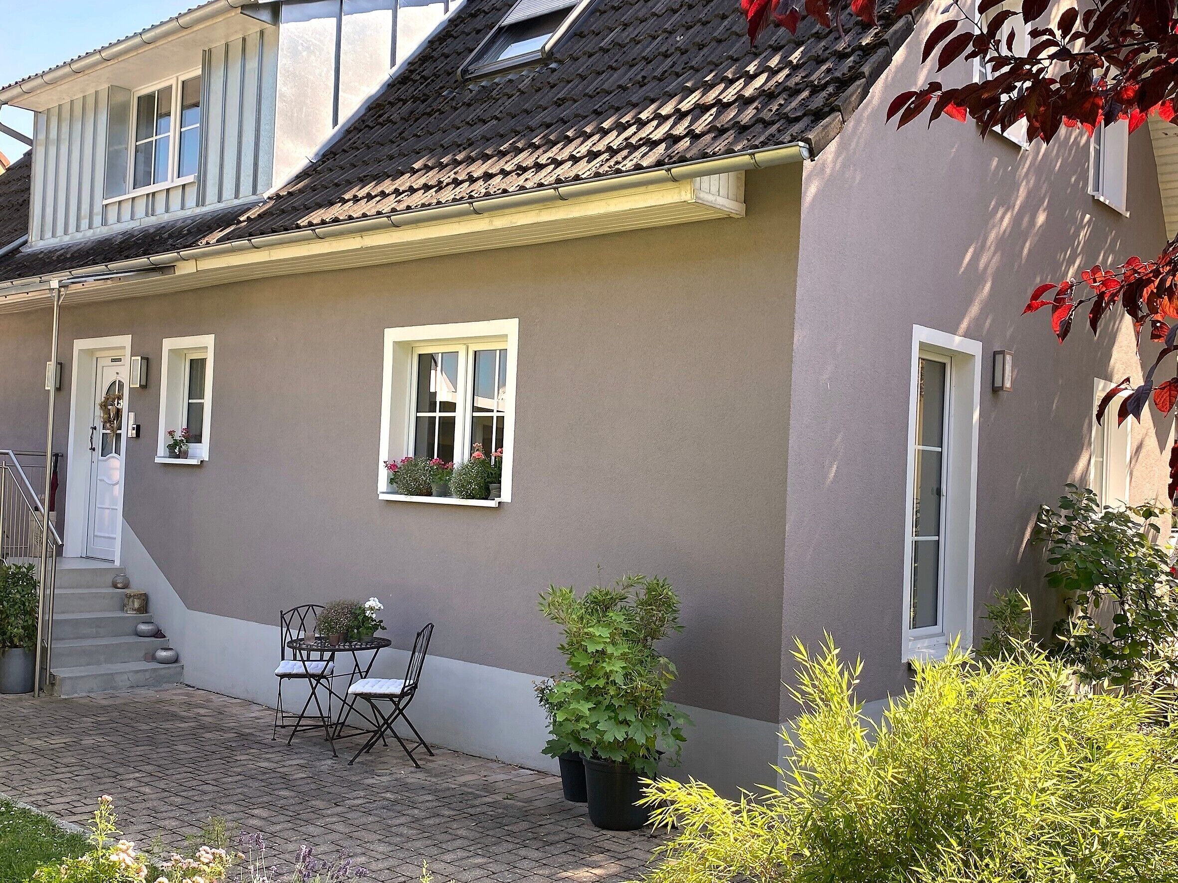 A house with a balcony, a small table with chairs, and potted plants.
