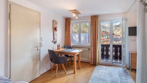 A room with a wooden table, two chairs, a bed, a radiator, a TV, and a balcony with a view of mountains. - Studio Apartment 'Haus Latschenhang 3 Soiernblick' with Mountain View, Balcony and Wi-Fi (Mittenwald)
