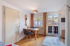 Une pièce avec une table en bois, deux chaises, un lit, un radiateur, une télévision et un balcon avec vue sur les montagnes.