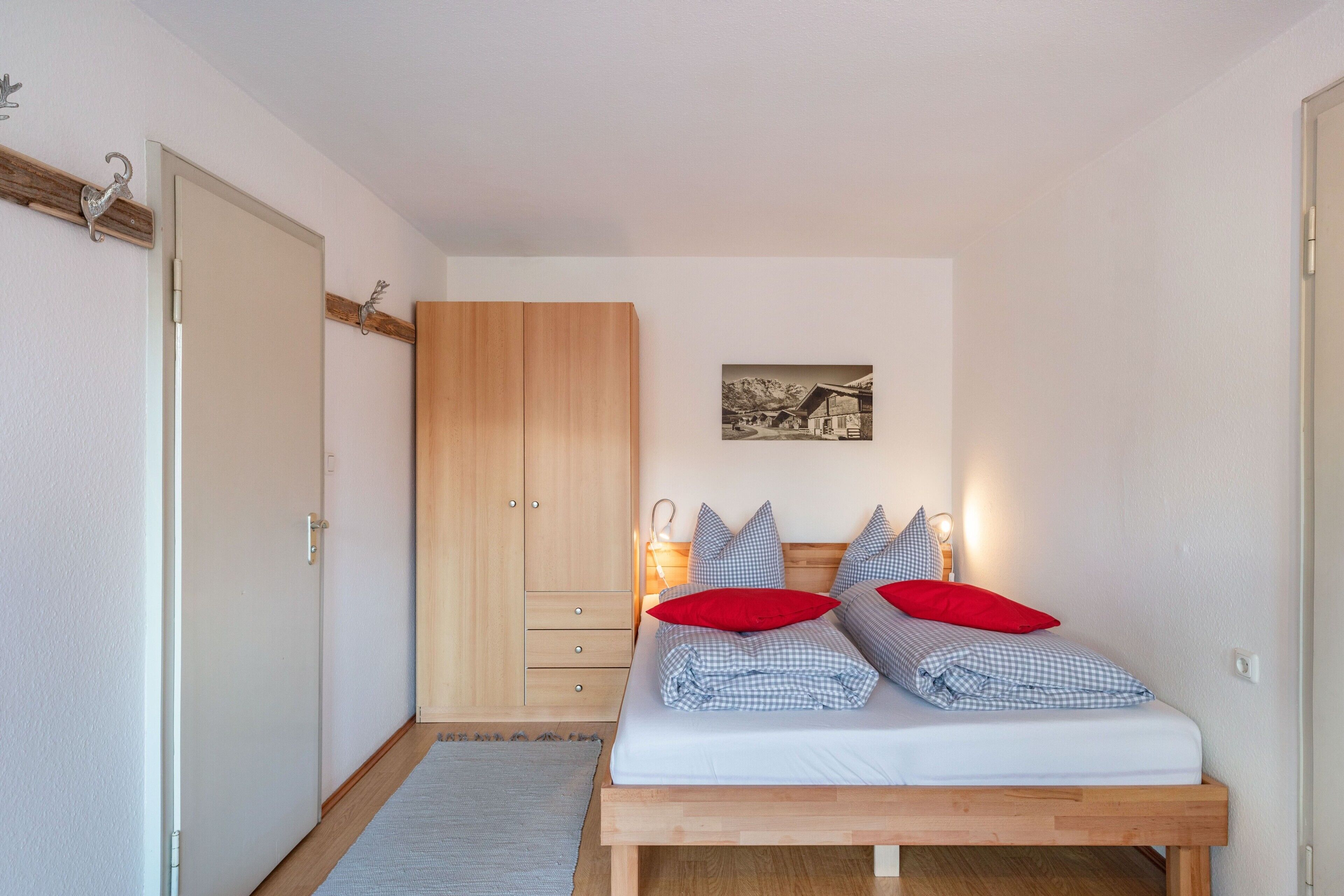 Ein Schlafzimmer mit einem Bett, einem Holzschrank, Nachttischlampen und einem gerahmten Bild an der Wand.