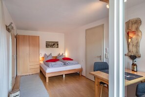 A bedroom with a bed, wooden wardrobe, desk, and chair.