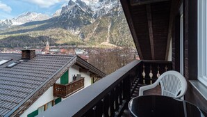 A balcony with a view of snow-capped mountains, a town below, and a white plastic chair. - Studio Apartment 'Haus Latschenhang 3 Soiernblick' with Mountain View, Balcony and Wi-Fi (Mittenwald)