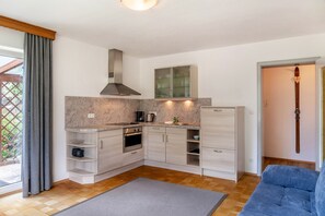 A compact kitchen with built-in appliances, a wooden floor, and a blue sofa in a bright room with a large window.