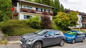 Ein zweistöckiges Gebäude mit Balkon, einem geparkten Auto davor und einem Baum mit gelben Blüten.