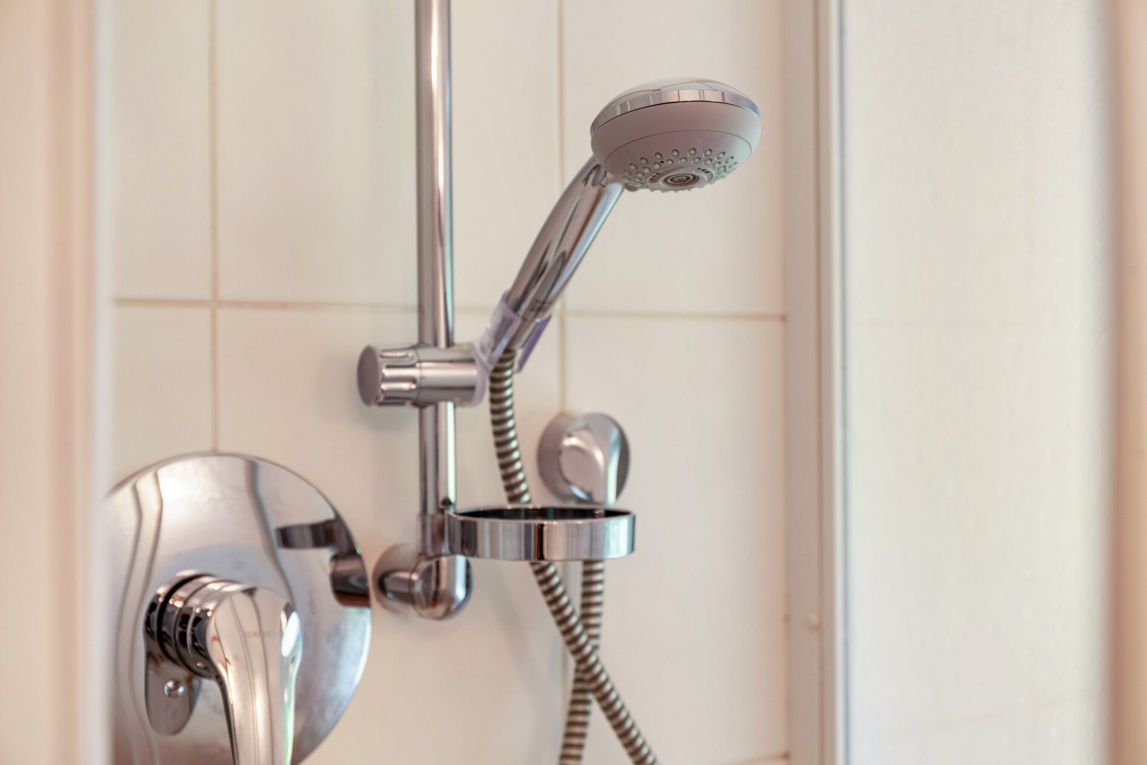 Une pomme de douche chromée avec un tuyau flexible, un robinet de commande fixé au mur et un robinet chromé.