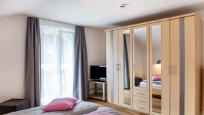 Ein Schlafzimmer mit Bett, Kleiderschrank, Schreibtisch mit Fernseher und einem Fenster mit Vorhängen.