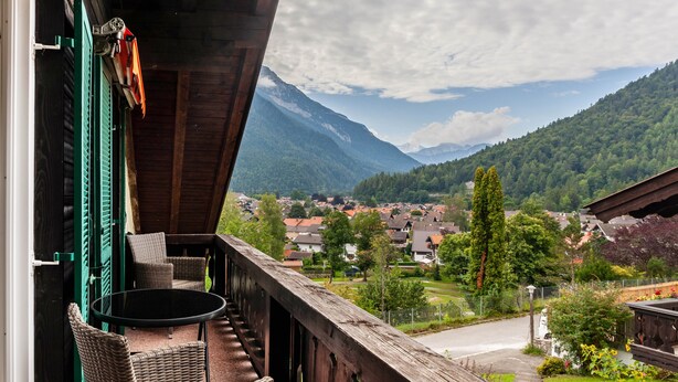 Ein Balkon mit Korbmöbeln, Blick auf eine Stadt und Berge im Hintergrund.