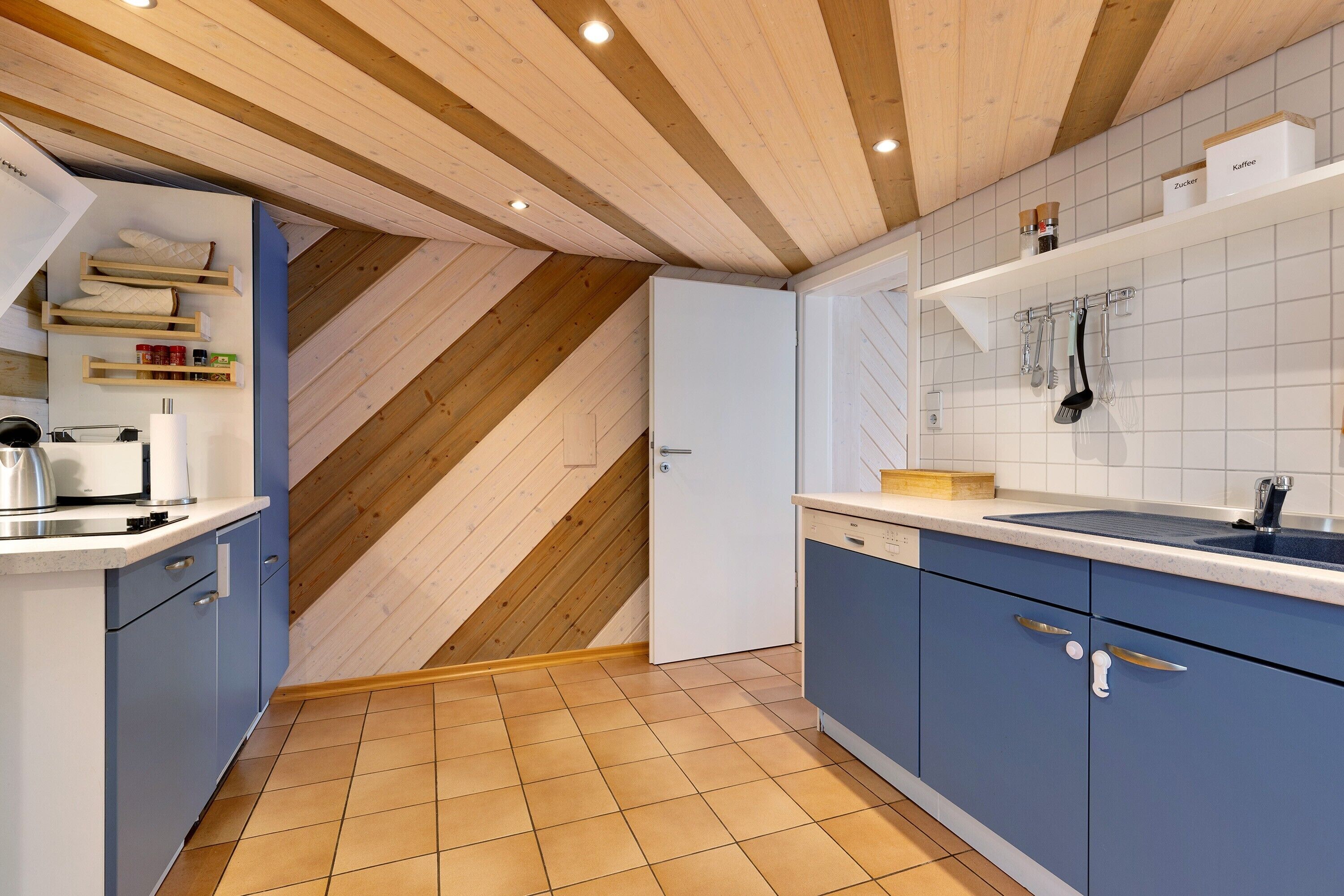 A kitchen with wooden beams, blue cabinets, a white countertop, and a tiled backsplash.
