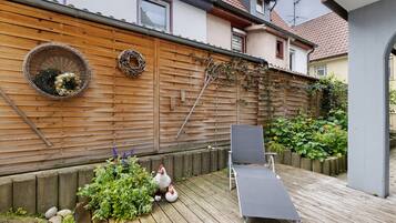 A wooden deck with a lounge chair, a wicker basket with flowers, and a garden wall.