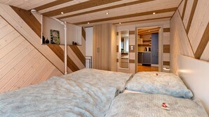 Een slaapkamer met twee bedden, houten balken in het plafond, een kitchenette en een badkamer.