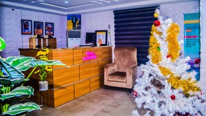 A reception area with a wooden desk, a plush armchair, a Christmas tree, and framed pictures on the wall. - Owee Hotel Exclusive Apartments & Suites (Lagos)