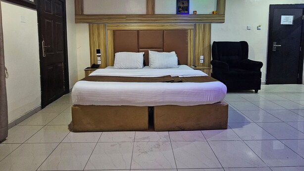 A hotel room with a large bed, a desk, a chair, and a wardrobe. - Owee Hotel Exclusive Apartments & Suites (Lagos)
