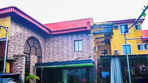 A multi-story building with a brick facade, a red roof, and a glass entrance. There are potted plants and a car parked in front. - Owee Hotel Exclusive Apartments & Suites (Lagos)