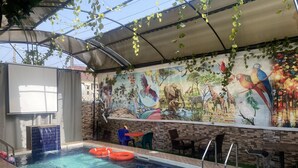 An indoor swimming pool with a mural of wildlife on the wall, surrounded by seating and a covered area with hanging plants. - Owee Hotel Exclusive Apartments & Suites (Lagos)