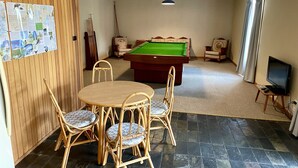 A room with a pool table, four wicker chairs, a television, and a ceiling fan.