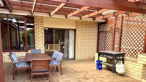 An outdoor patio with a wooden table and chairs, a grill, and a propane tank.
