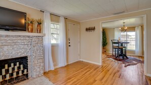 A living room with a fireplace, wooden flooring, a flat-screen TV, and a dining area with a table and chairs. - Rusk Retreat w/ Fire Pit, Grill & Countryside View (Rusk)