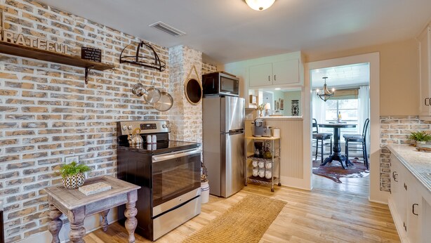 A modern kitchen with a brick wall, stainless steel appliances, and a wooden table with a plant. - Rusk Retreat w/ Fire Pit, Grill & Countryside View (Rusk)