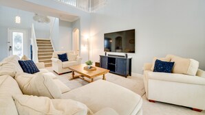 A spacious living room with a high ceiling, a staircase, a flat-screen TV, and a large beige sofa.