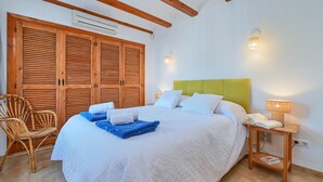A bedroom with a large bed, wooden wardrobe, wicker chair, bedside table with lamp, and wall-mounted light. - Wonderful and comfortable villa  with private pool in Javea, Costa Blanca, Spain for 6 persons (Javea)