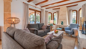 A cozy living room with a sofa, armchairs, and a coffee table. There are large windows with curtains, a lamp, and a decorative vase. - Wonderful and comfortable villa  with private pool in Javea, Costa Blanca, Spain for 6 persons (Javea)