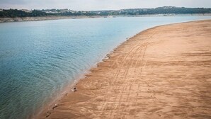 Ein weiter Sandstrand mit klarem, blauen Wasser und einer entfernten Küstenlinie mit Gebäuden.