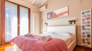 Ein Schlafzimmer mit einem großen Bett, einem Fenster mit Jalousien, einem Heizkörper und einer Wand-Klimaanlage.