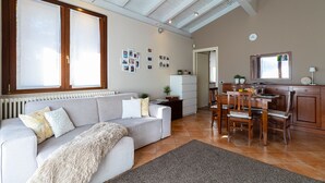 Ein modernes Wohnzimmer mit einer Couch, einem Esstisch und Stühlen. Es gibt eine Küchenzeile mit Schränken und einem Kühlschrank.