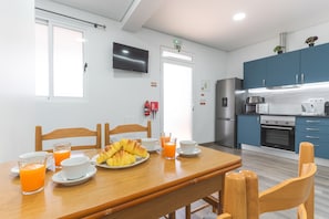 A breakfast setup with croissants, orange juice, and coffee on a wooden table in a modern kitchen with blue cabinets and a flat-screen TV. - Gomes House by Atlantic Holiday (Ponta do Sol)