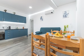 A modern kitchen with blue cabinets, a dining table with chairs, and a sofa in the living area. - Gomes House by Atlantic Holiday (Ponta do Sol)