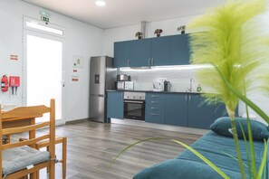 A modern kitchen with blue cabinets, stainless steel appliances, and a wooden dining area with a chair.