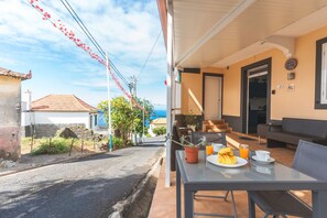 Un patio exterior soleado con una mesa lista para el desayuno, un sofá y una escalera que lleva a un nivel superior.