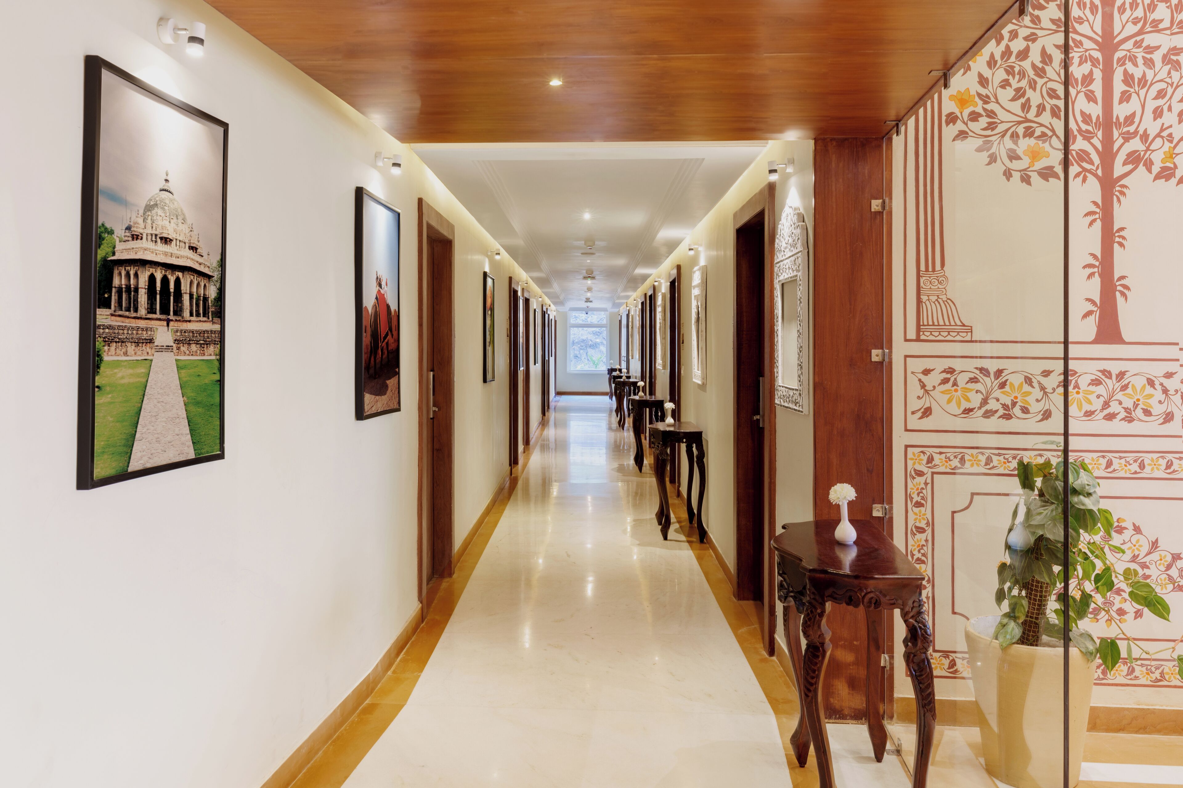 A hotel corridor with framed pictures on the walls, a polished floor, and a wooden ceiling.