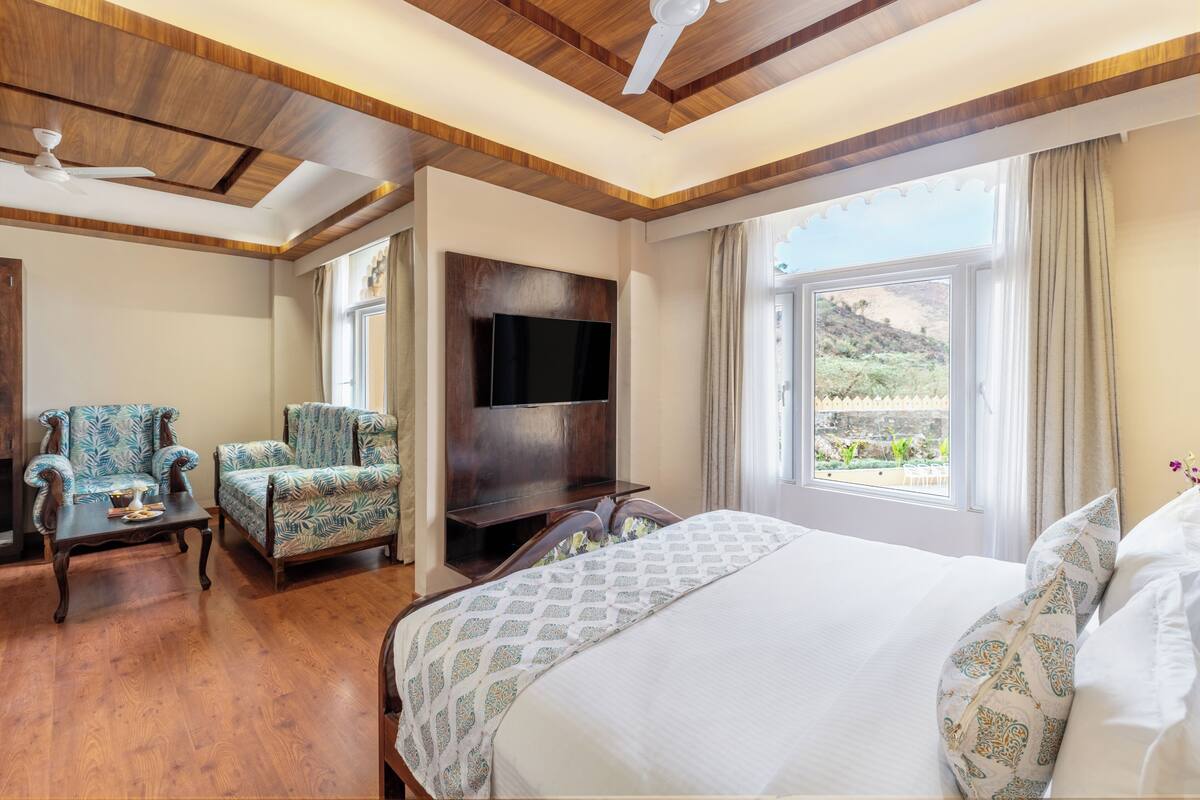 A hotel room with a large bed, a TV mounted on the wall, a ceiling fan, and a view of the outdoors.
