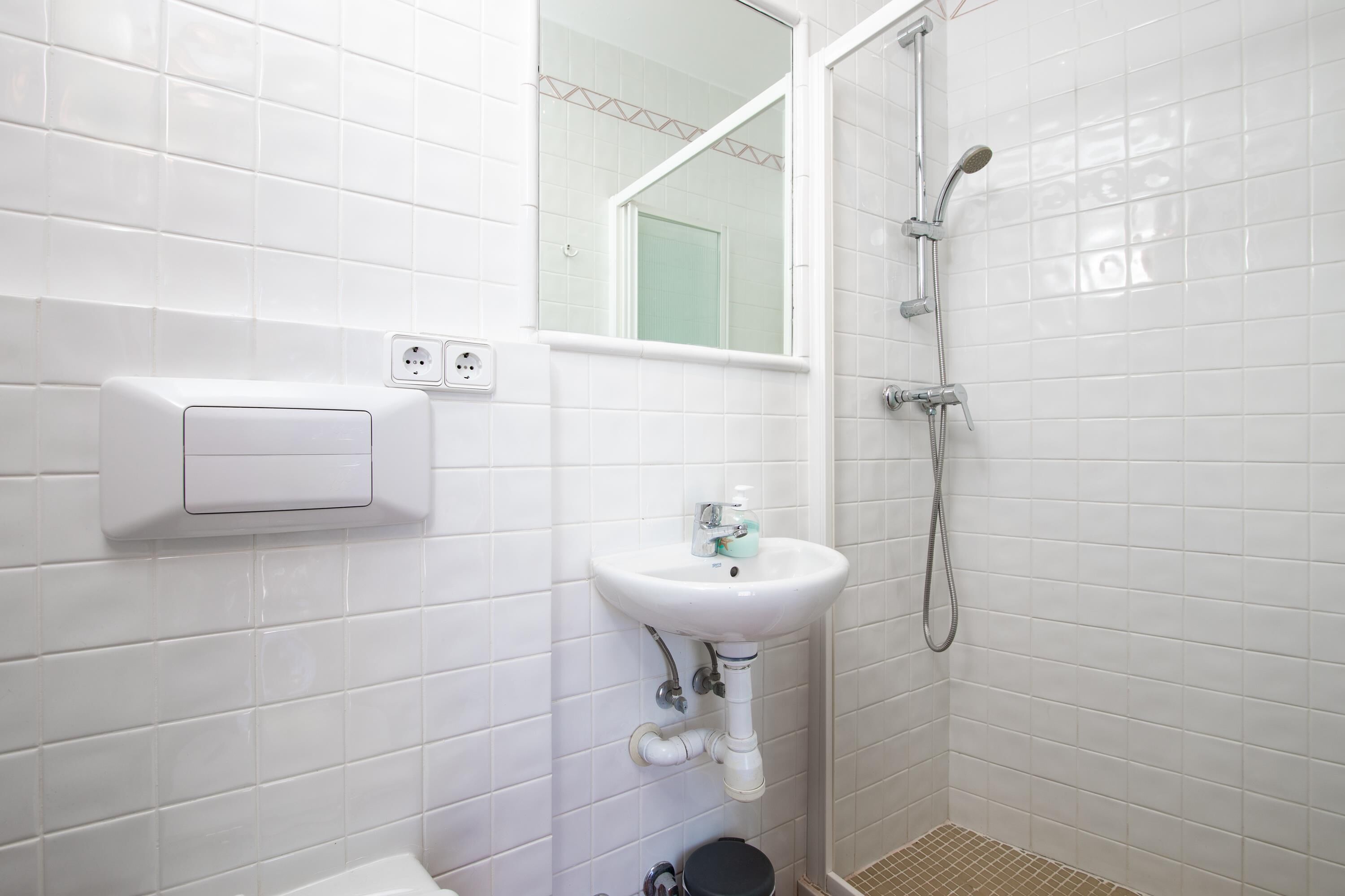 A bathroom with white tiled walls, a white sink with a mirror above it, and a shower with a handheld showerhead.
