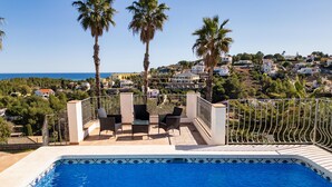 A swimming pool with a tiled edge, surrounded by outdoor furniture and palm trees. - Castillo de Troya - Denia, Costa Blanca (Denia)